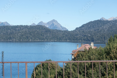 Relaxing blue lake with mountain range and dense forests behind, view from balcony with thin wooden railings