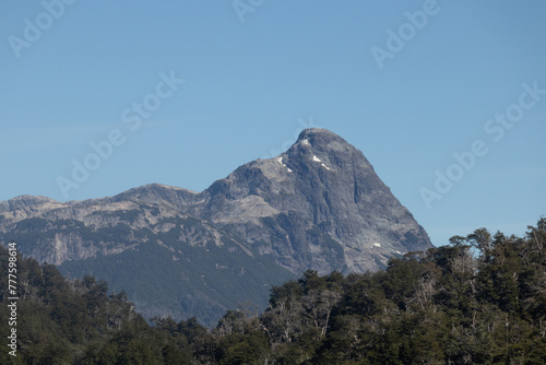 Lonely horizontal view of mountain peak with growing vegetation on the bottom, and an infinite clear blue sky on top