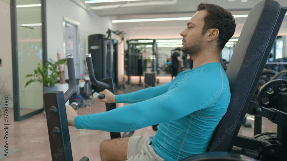 Middle-aged athletic man performs exercises on chest press machine. Chest workout. Sportsman holds handles, pushes outwards and fully extends arms - side view medium shot Middle-aged athletic man performs exercises on chest press machine. Chest workout. Sportsman holds handles, pushes outwards and fully extends arms - side view medium shot
