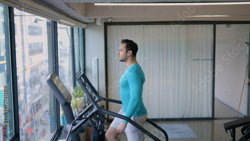 Fit Male Exercises on Stepmill Stair Climber Machine in Modern Gym While Enjoying City Street View Through Window - Medium Wide photo