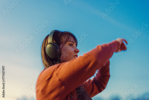 Young woman wears headphones and dances to music at sunset. photo