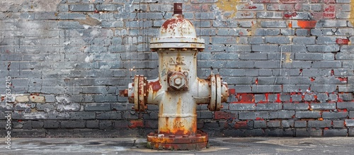 A weathered white fire hydrant covered in red rust stands in front of a textured brick wall, showcasing urban decay and neglect. photo