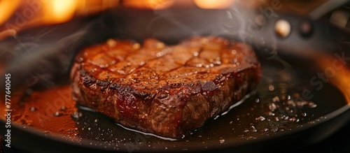 A heart-shaped steak is sizzling and cooking in a hot frying pan on a stovetop.