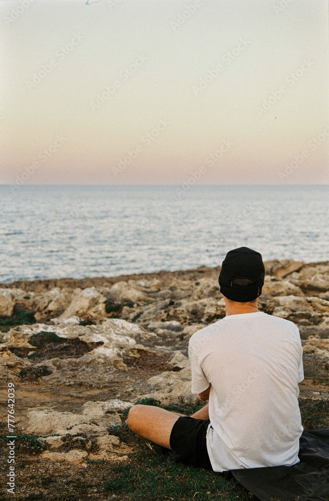 Anonymous young man sitting on the rocks near the sea Anonymous young man sitting on the rocks near the sea