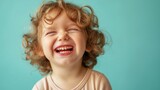 Cheerful little toddler or little curly child laughing on blue background
