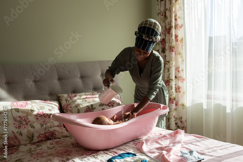Smiling mother washing baby in bath in bedroom  photo