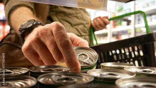 Close-up of a male buyers hand with a shopping basket taking a small tincan in a supermarket photo