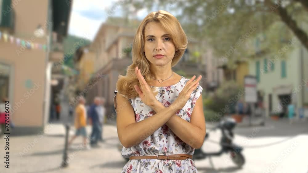 Portrait of a serious blond woman standing outdoors cross her arms as a sign of prohibition. City street in the background. Portrait of a serious blond woman standing outdoors cross her arms as a sign of prohibition. City street in the background.