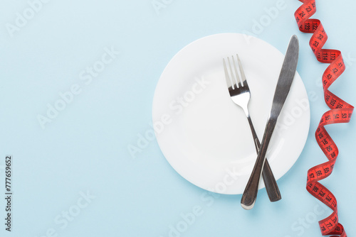 Measuring tape with empty plate on wooden background, top, view. Weight loss concept