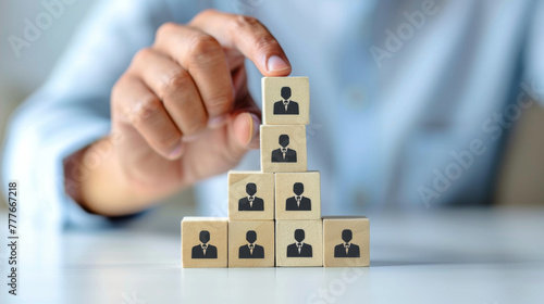 A hand stacking wooden blocks in a pyramid shape, each block featuring a person icon.