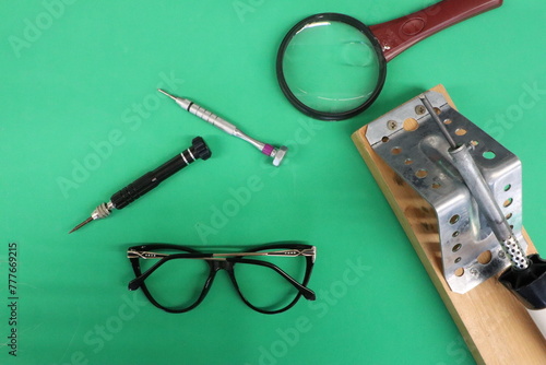 Various electronic components and tools are on a green table repair of eyeglasses for vision