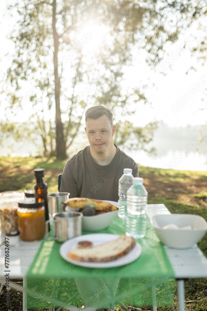 young man with down syndrome camping in nature having breakfast young man with down syndrome camping in nature having breakfast