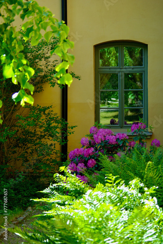 Yellow stone building exterior with a lattice window with reflections behind a flowering garden.  photo