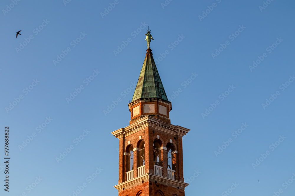 Close up view at sunrise of bell tower of Church of Saint James Apostle in charming town of Chioggia, Venetian Lagoon, Veneto, Italy. Sightseeing in historic old town. First sun beams on landmark