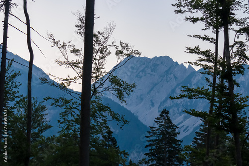 Scenic view of mountain peak Veliki Vrh (Hochturm) in untamed Karawanks, border Austria Slovenia, Europe. Hiking on Loibl Pass in Slovenian Alps venturing through tranquil forest in early morning photo