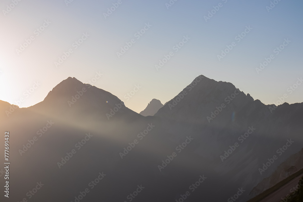 Panorama of stunning sunrise with golden sun beams over majestic summits of untamed Karawanks mountain range. Vantage point of Loibl Pass, border Austria Slovenia. First rays of morning sun in Alps