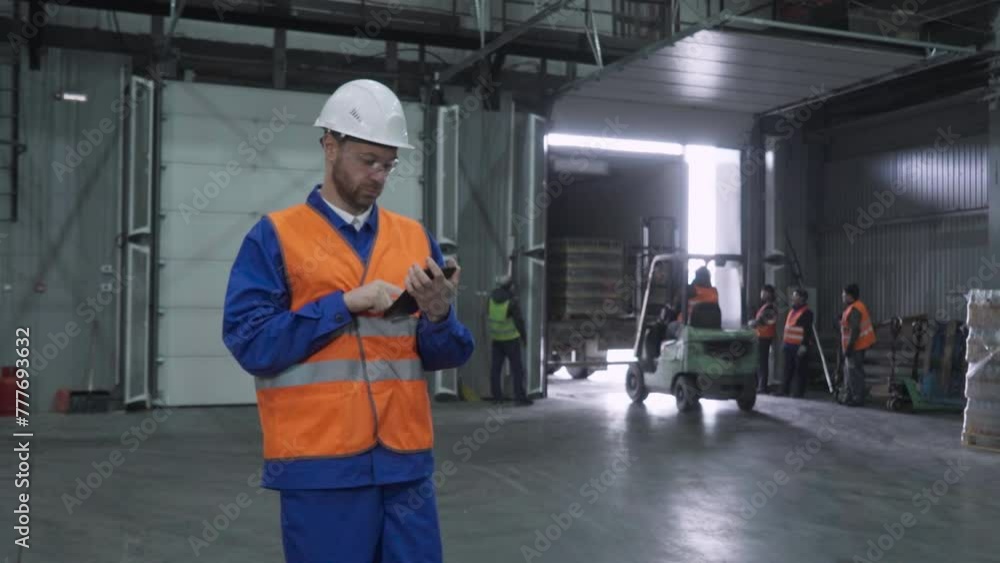 Storehouse inspector with a tablet supervises the workers on trucks. Worker with a tablet observing the trucks moving supply pallets. Worker pressing buttons on tablet screen. Industrial trucks. Storehouse inspector with a tablet supervises the workers on trucks. Worker with a tablet observing the trucks moving supply pallets. Worker pressing buttons on tablet screen. Industrial trucks.