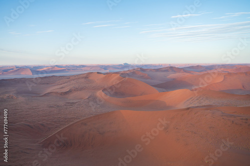 Breathtaking sunrise over the sand dunes of Sossusvlei, Namibia, captured from a helicopter. The first light of dawn casts dramatic shadows and highlights the vibrant colors of the desert.