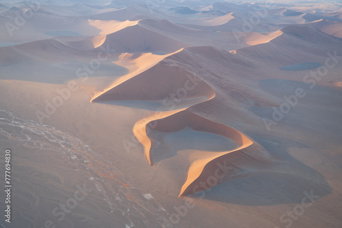 Breathtaking sunrise over the sand dunes of Sossusvlei, Namibia, captured from a helicopter. The first light of dawn casts dramatic shadows and highlights the vibrant colors of the desert.