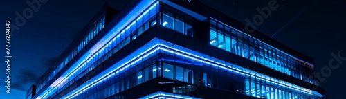 A contemporary office building illuminated with blue lights against the night sky