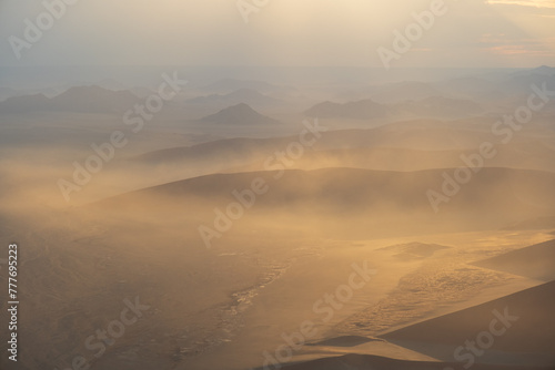 Breathtaking sunrise over the sand dunes of Sossusvlei, Namibia, captured from a helicopter. The first light of dawn casts dramatic shadows and highlights the vibrant colors of the desert.