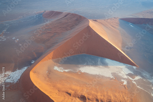 Breathtaking sunrise over the sand dunes of Sossusvlei, Namibia, captured from a helicopter. The first light of dawn casts dramatic shadows and highlights the vibrant colors of the desert.