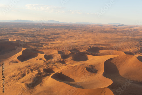 Breathtaking sunrise over the sand dunes of Sossusvlei, Namibia, captured from a helicopter. The first light of dawn casts dramatic shadows and highlights the vibrant colors of the desert.