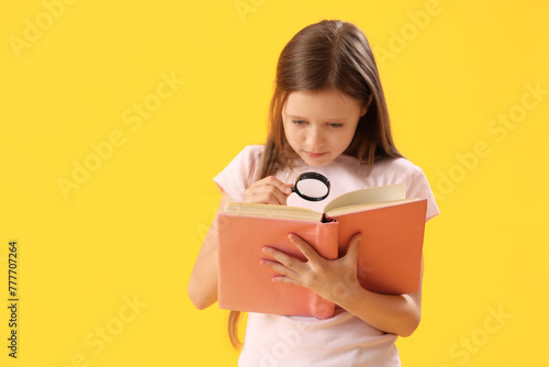 Little girl with magnifier and book on yellow background