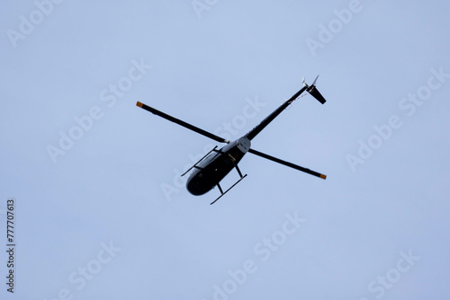 A black helicopter crosses the blue sky with clouds. Transportation. Urban.