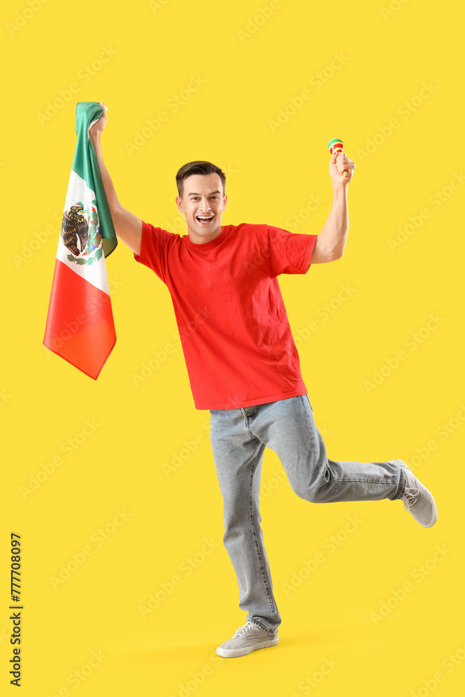 Handsome man with Mexican flag and maraca dancing on yellow background Handsome man with Mexican flag and maraca dancing on yellow background