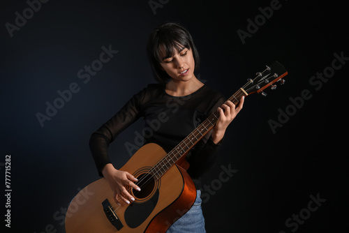 Cool young woman playing guitar on black background