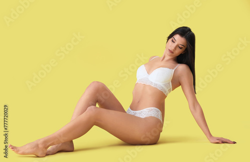 Beautiful young woman in white lace underwear sitting on yellow background