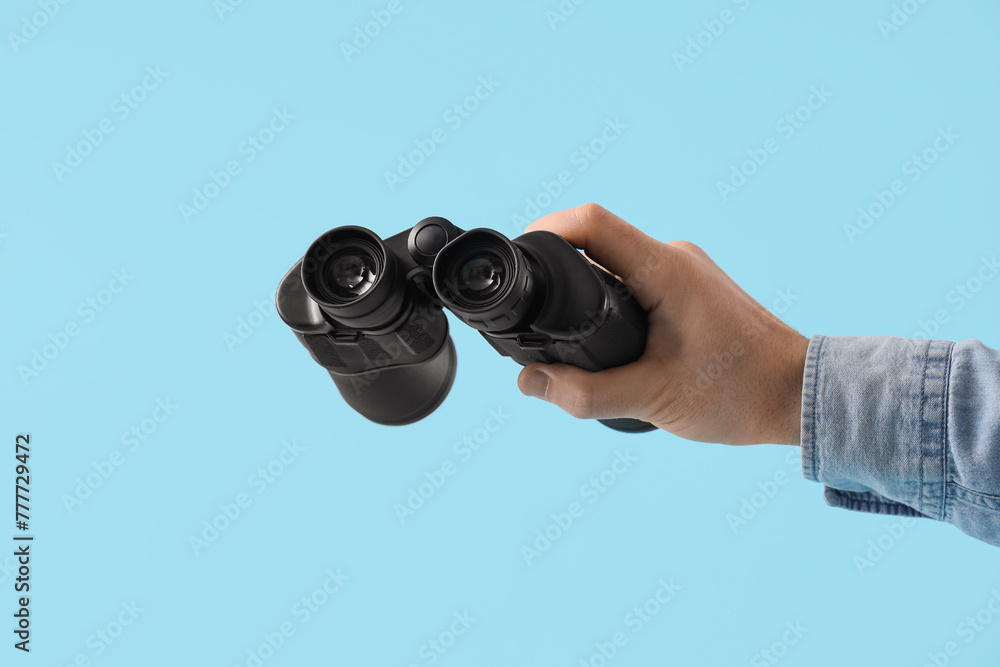 Male hand holding binoculars on blue background, closeup Male hand holding binoculars on blue background, closeup
