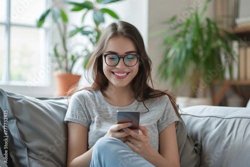 Smiling young woman using smart phone sitting on couch
