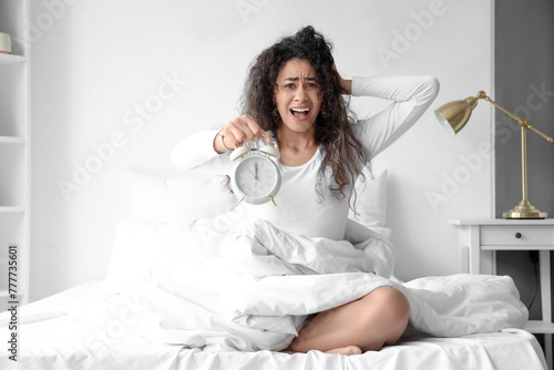 Overslept young African-American woman with alarm clock in bedroom photo