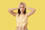 Tired young woman suffering from headache on yellow background