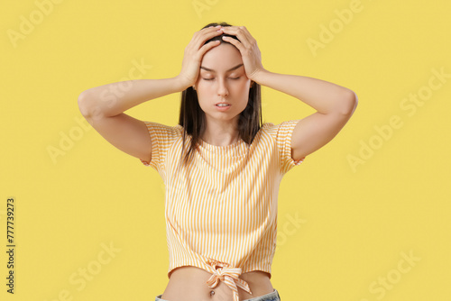 Tired young woman suffering from headache on yellow background © Pixel-Shot