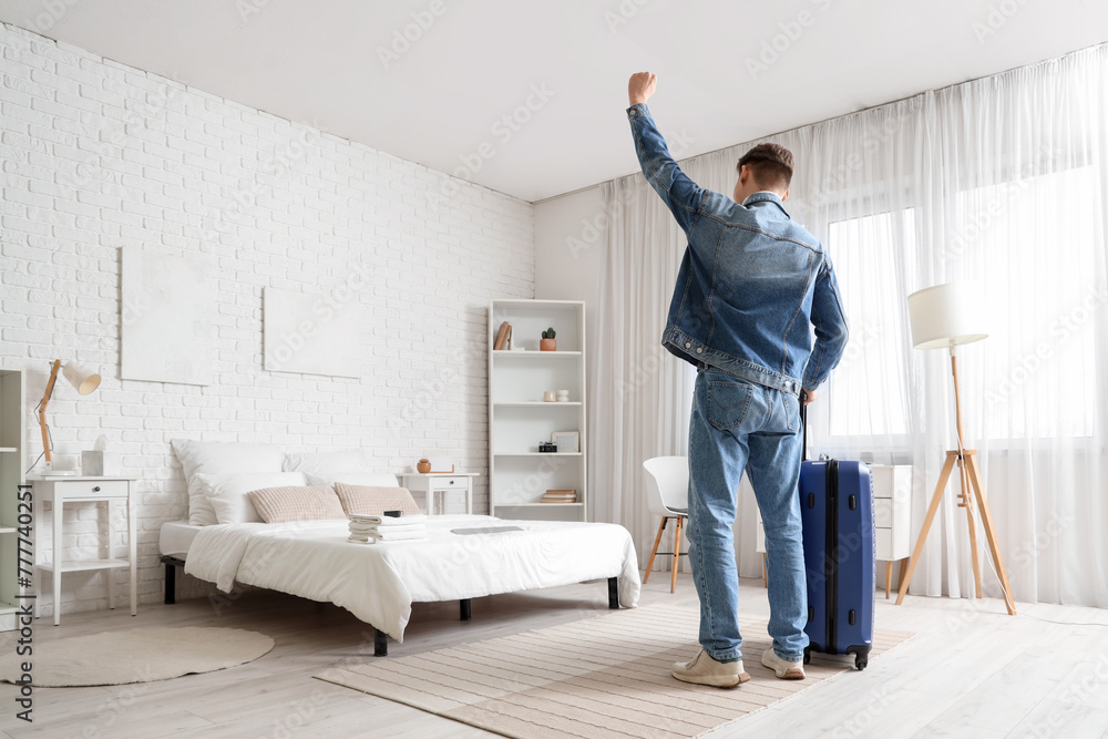 Happy male tourist with suitcase in hotel room, back view