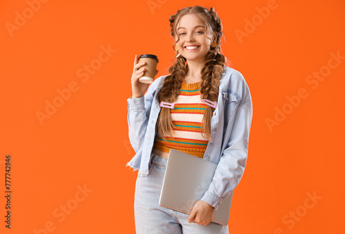 Happy smiling young woman with braids holding laptop and cup of coffee on orange background
