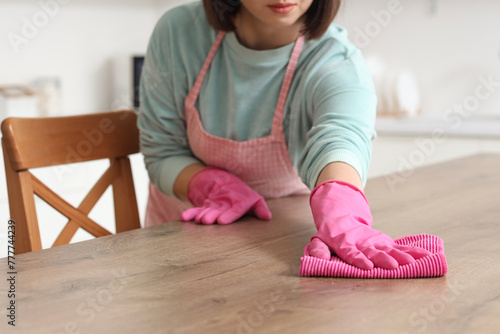 Woman cleaning wooden table with rag in kitchen, closeup