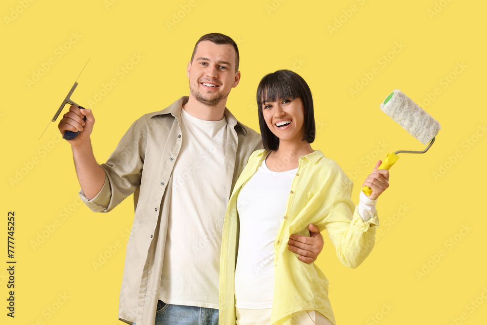 Young couple with trowel and paint roller hugging on yellow background. Repair concept