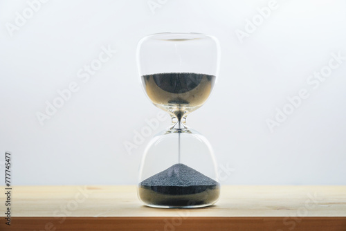 Hourglass with black sand on a wooden table against a light gray background, concept for time passing by, seize the day and enjoy the moment, copy space