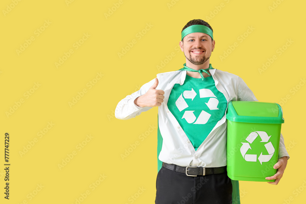 Young man dressed as eco superhero with garbage bin showing thumb-up on yellow background. Ecology concept Young man dressed as eco superhero with garbage bin showing thumb-up on yellow background. Ecology concept