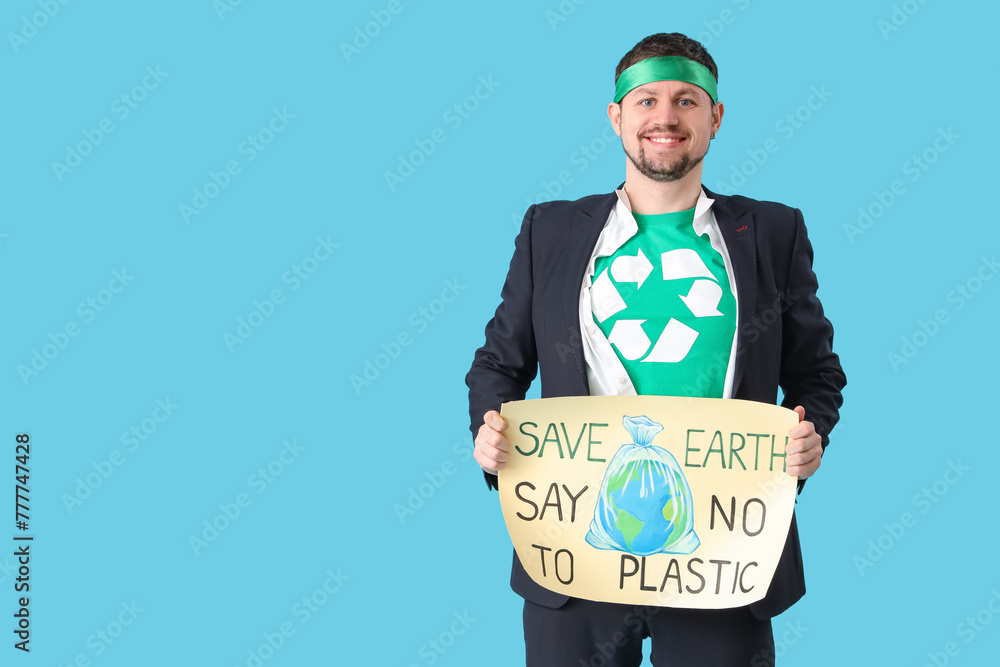 Young man dressed as eco superhero holding poster with text SAVE EARTH SAY NO TO PLASTIC on blue background. Ecology concept - obrazy, fototapety, plakaty 