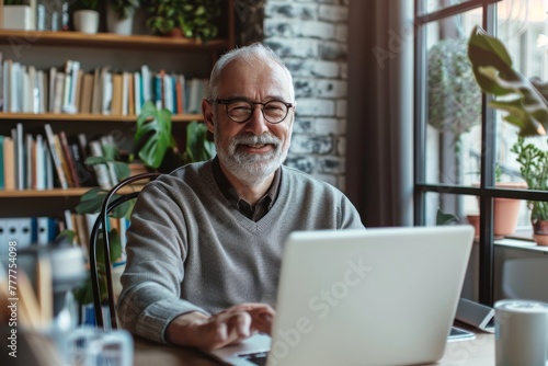 A man in a gray sweater is sitting at a desk with a laptop in front of him