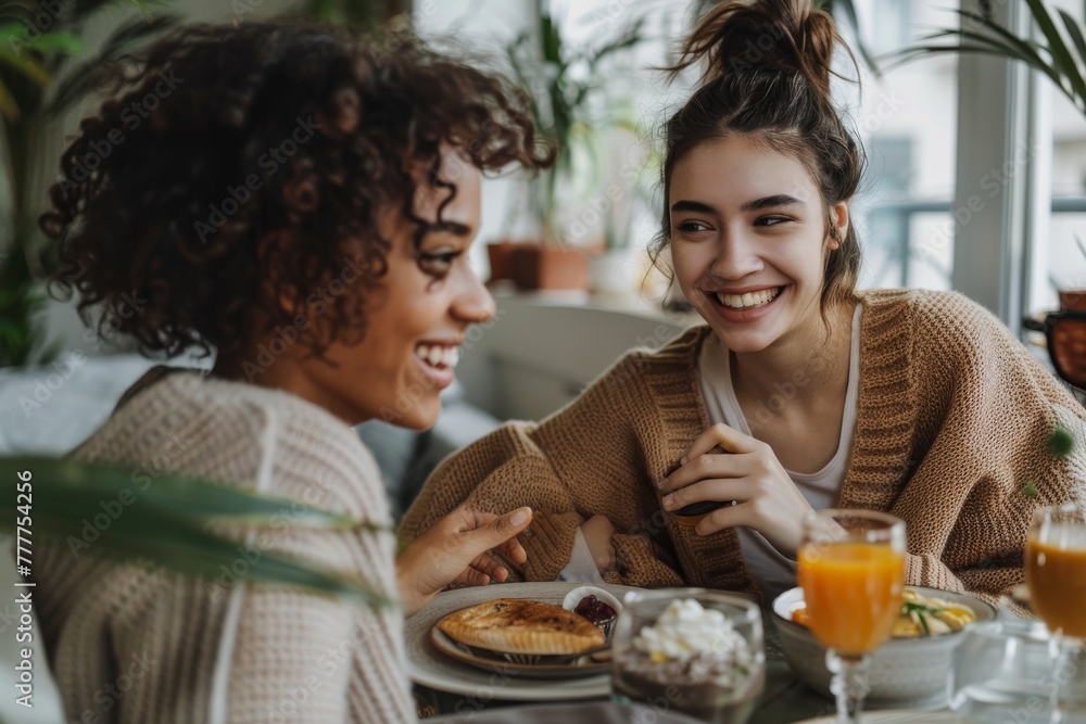 Two women are sitting at a table, smiling and laughing while eating breakfast