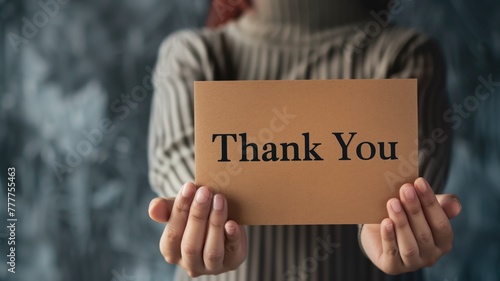 Person holding "Thank You" sign in front of them, wearing turtleneck sweater