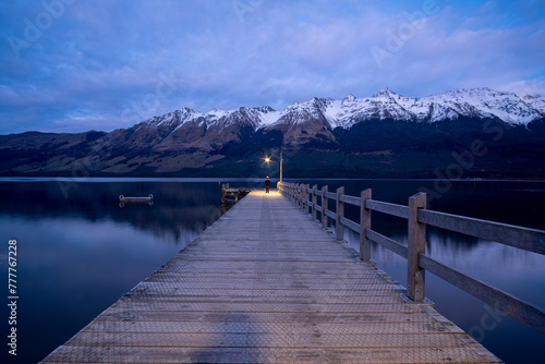 Boy standing under lamp at the end of a Jetty with mountain reflection photo
