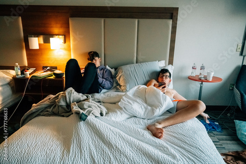 Teen boys laying in a bed on their phones.  photo