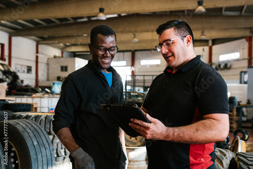 Positive multiracial mechanic male colleagues holding tablet in garage photo